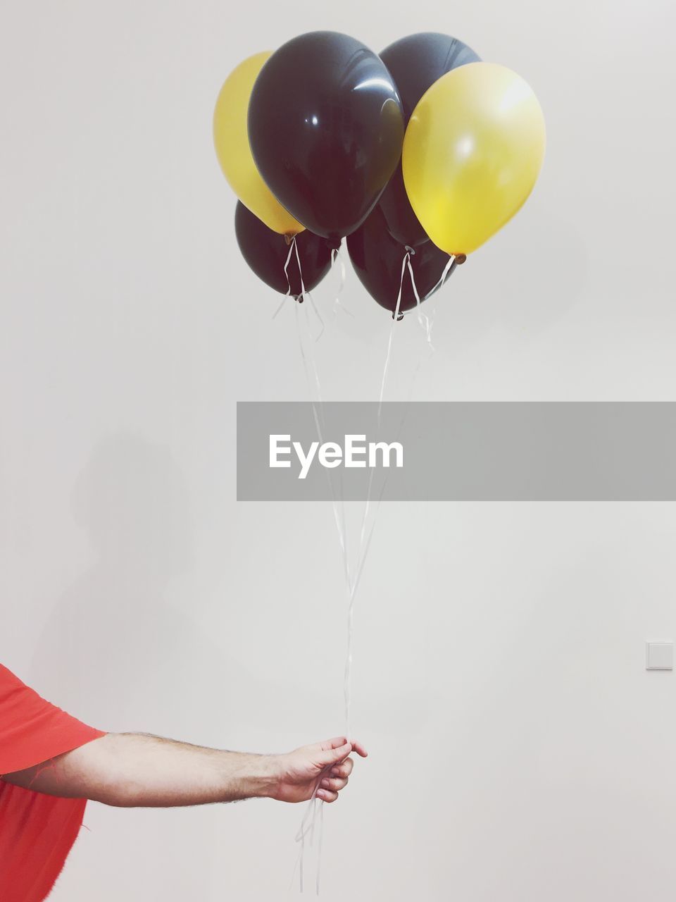 Close-up of hand holding balloons against wall