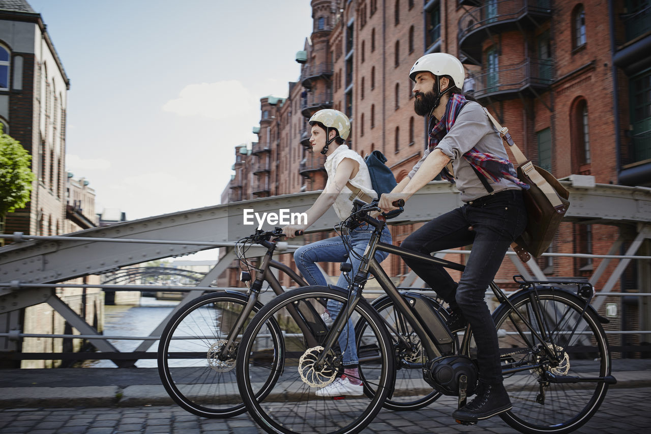 Germany, hamburg, couple riding electric bicycles at old warehouse district