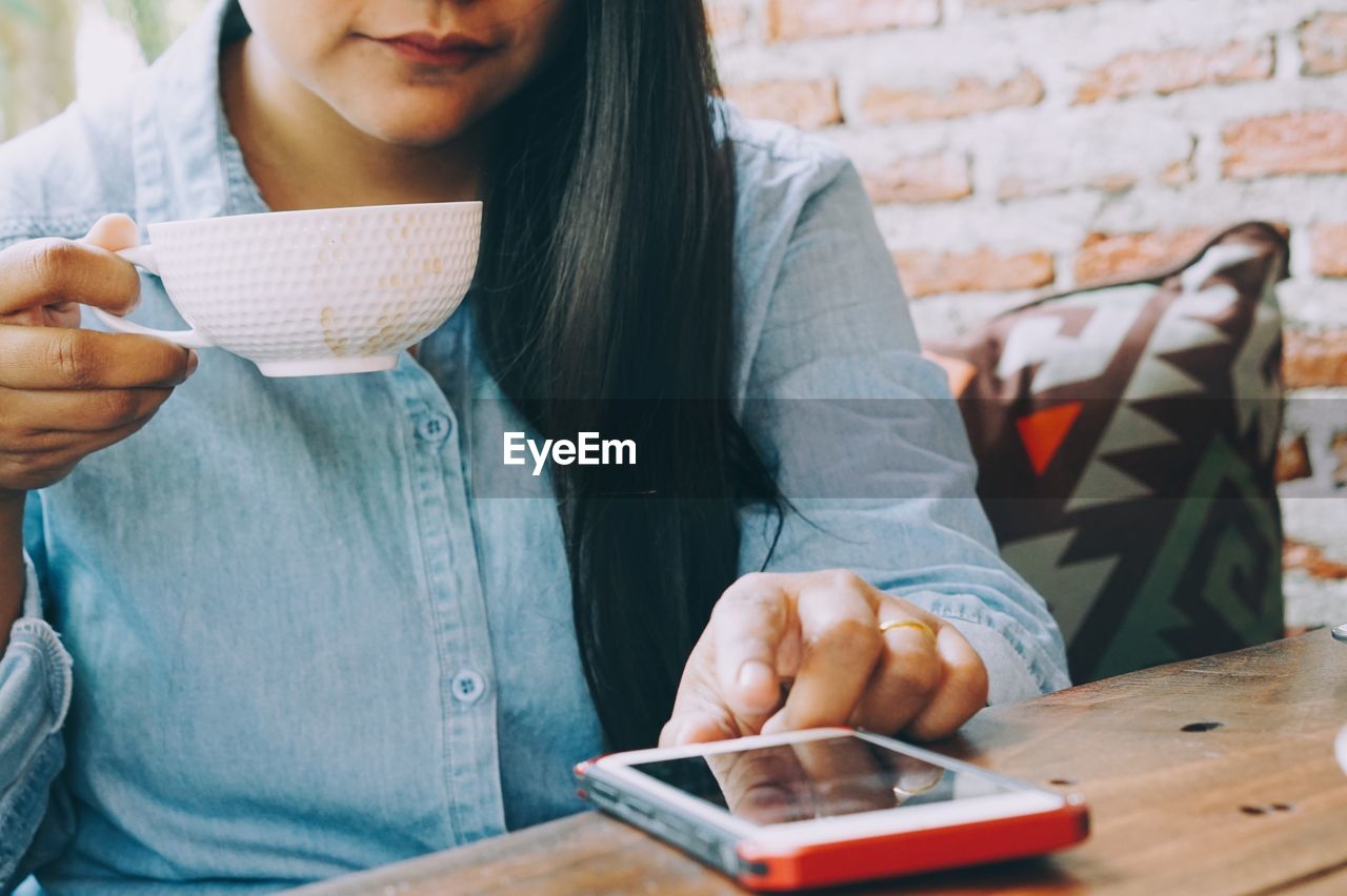 Midsection of woman having drink while using smart phone at table in cafe