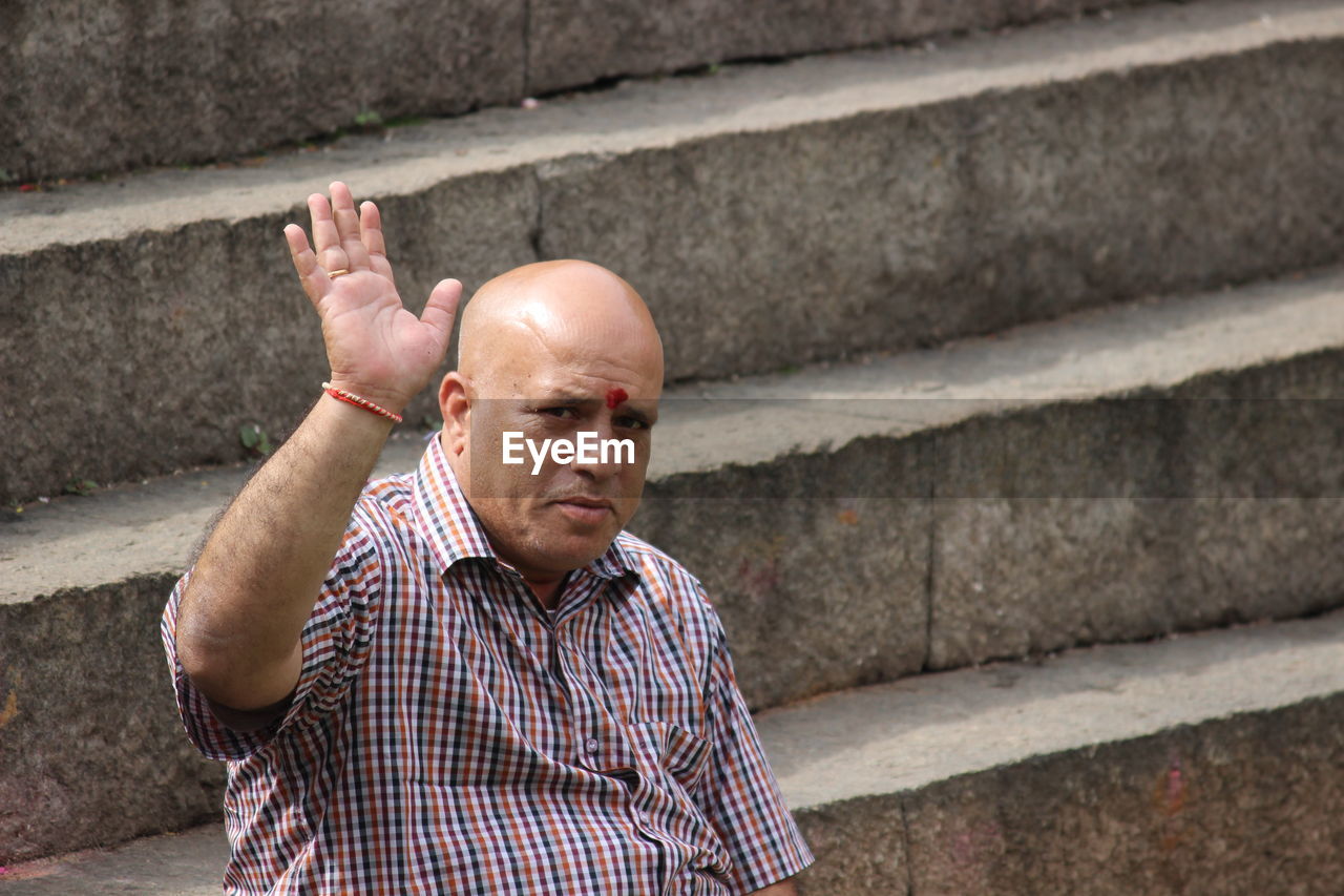 Portrait of man waving hand while sitting on steps