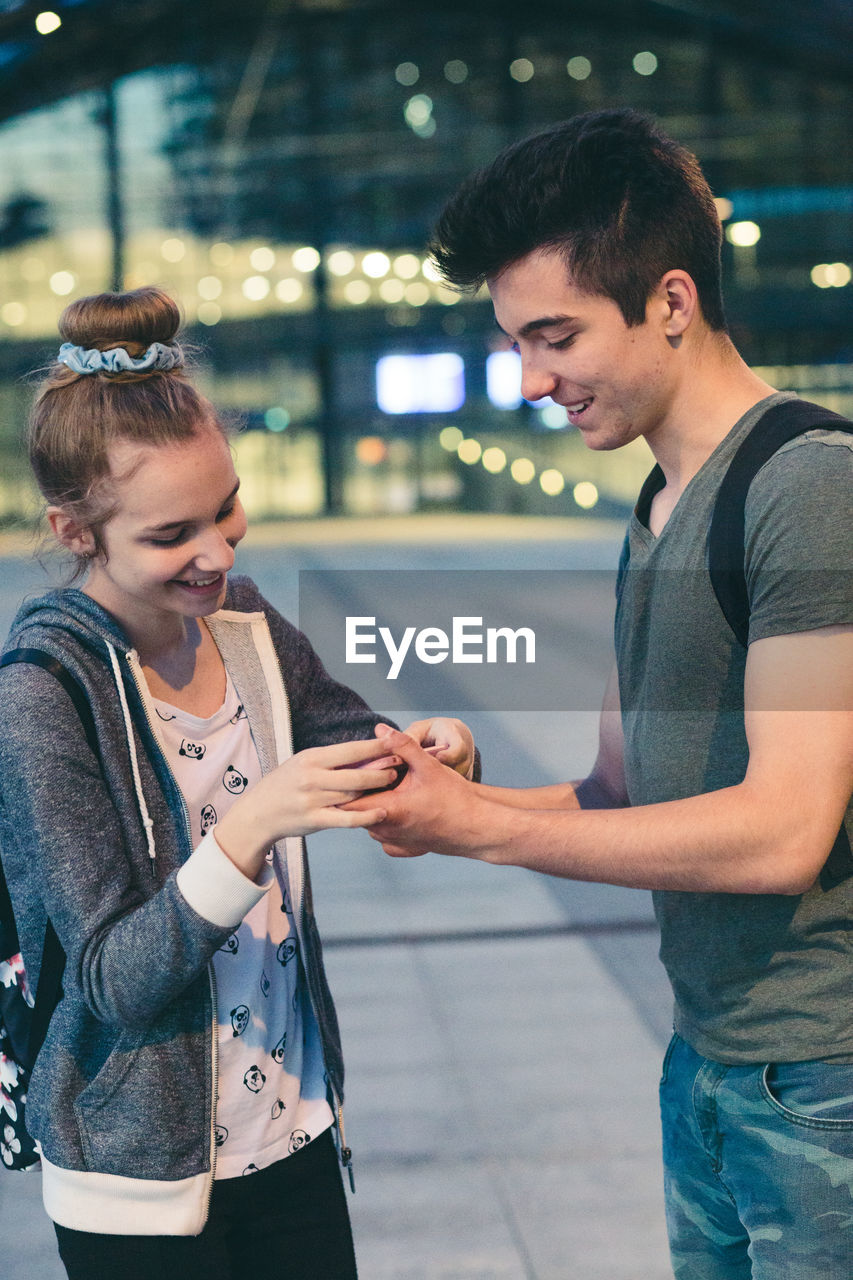 Full length of teenage couple looking at mobile phone in airport