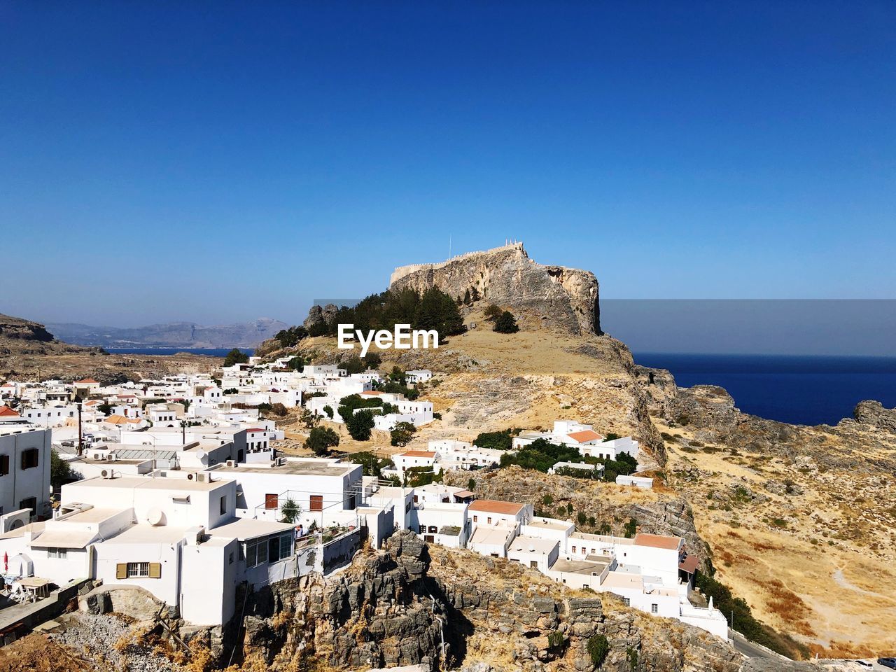 Buildings by sea against clear blue sky