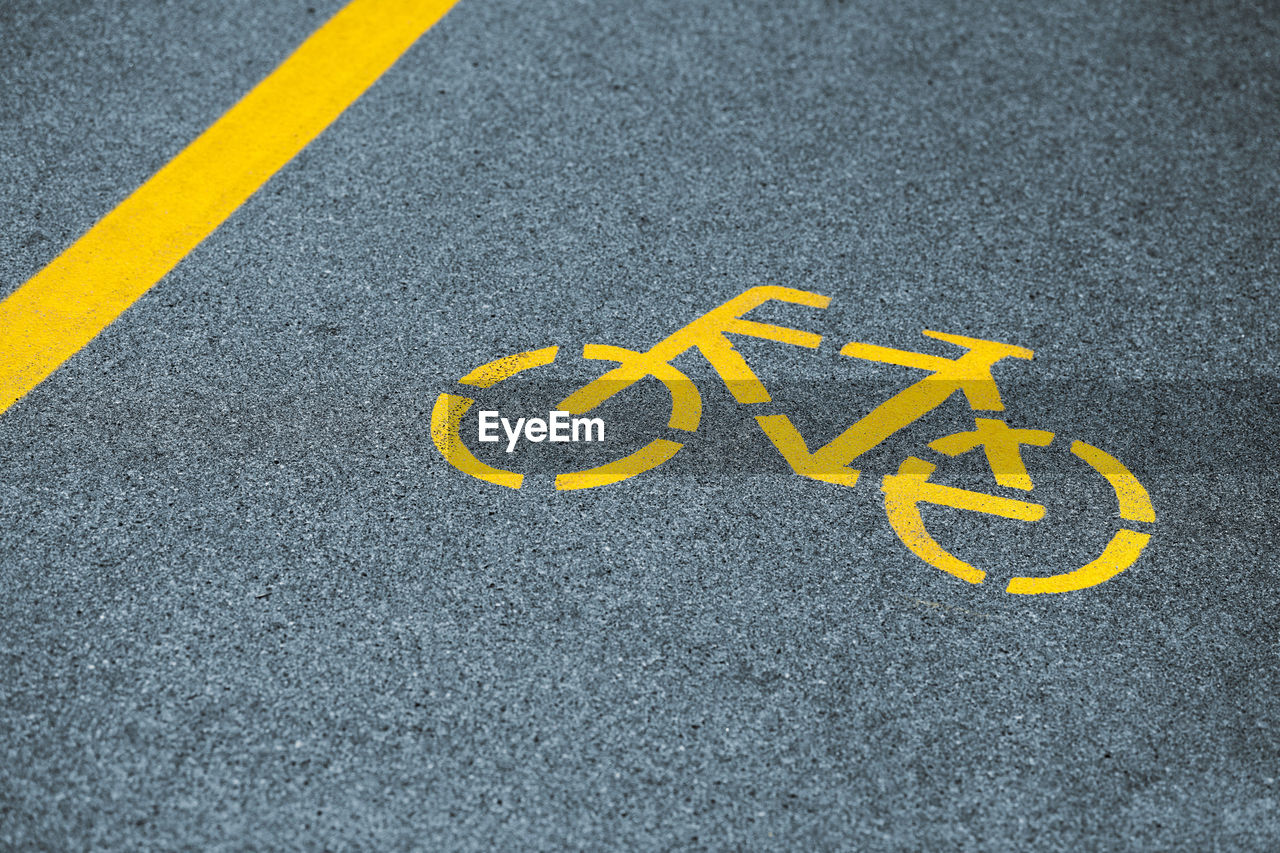 Yellow bicycle sign on cycling path, safe road traffic near highway. painted bicycle road sign
