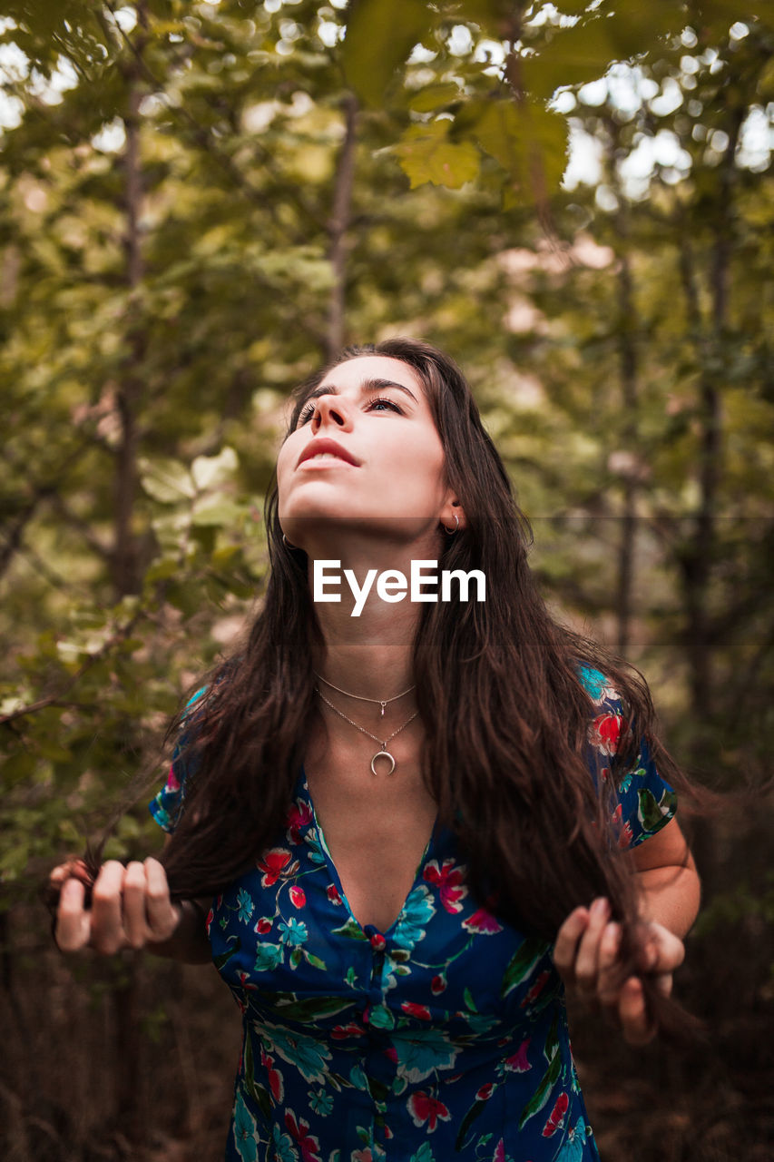 Woman looking up while standing against trees