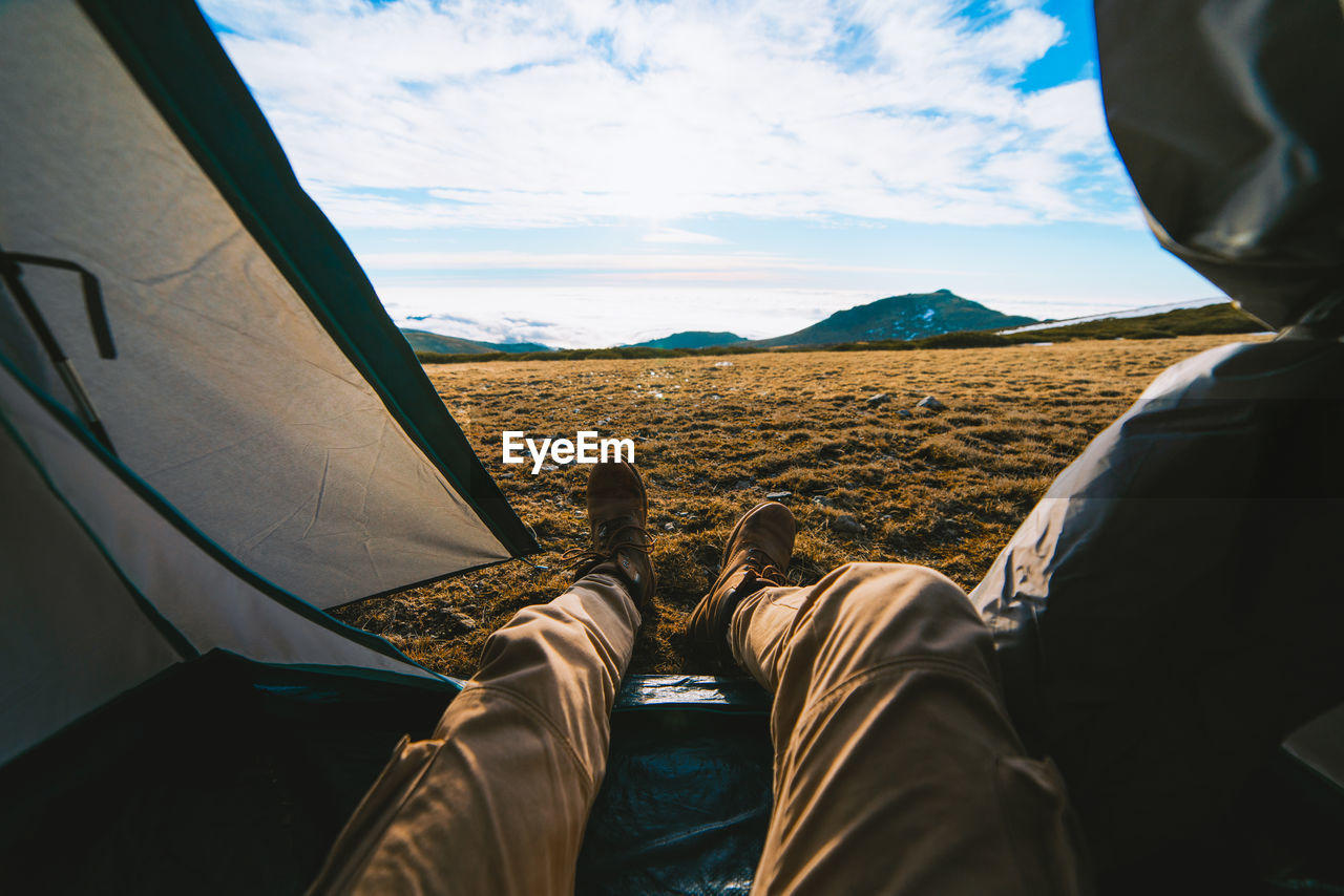 Crop unrecognizable male traveler in casual clothes lying in camping tent and admiring picturesque mountain landscape on sunny day