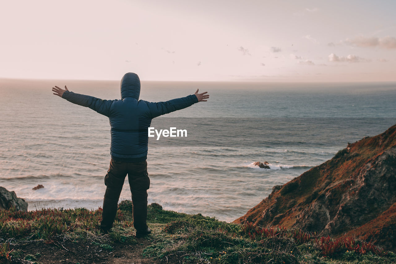 Full length of man with arms outstretched standing against beach during sunset