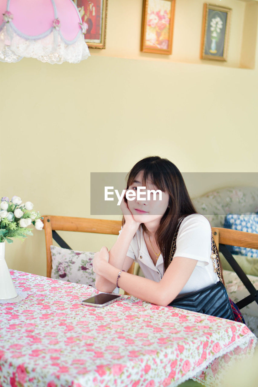 portrait of young woman using mobile phone while sitting on bed at home