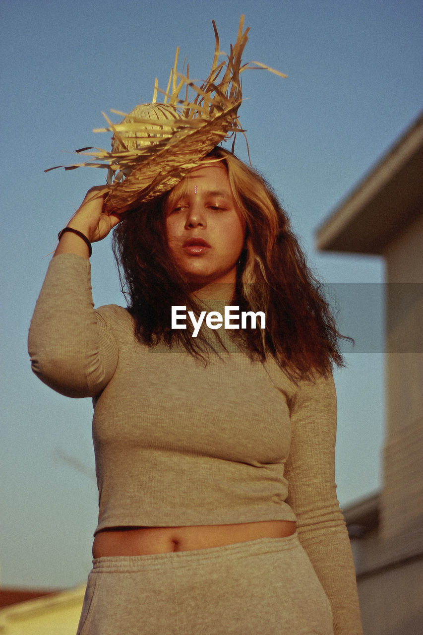 Young woman with wicker basket standing against sky