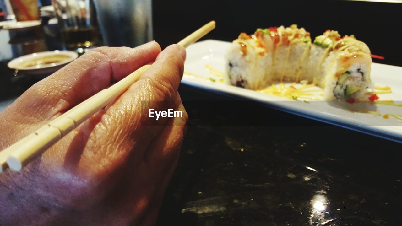 Cropped image of hand holding chopsticks by sushi in plate