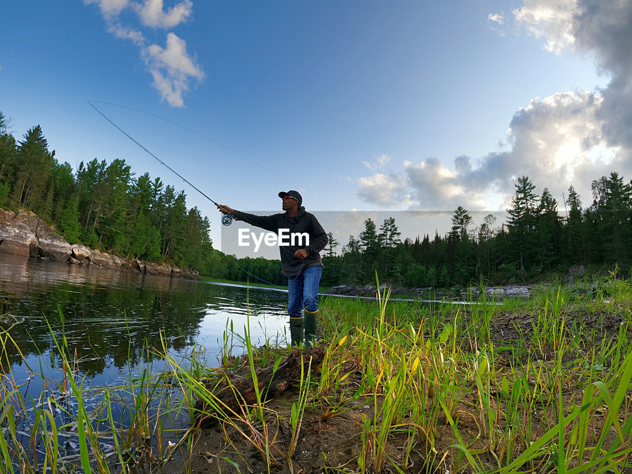 sky, one person, plant, nature, adult, water, men, cloud, activity, rural area, leisure activity, landscape, full length, land, tree, lake, beauty in nature, grass, rural scene, standing, scenics - nature, environment, lifestyles, fishing, tranquility, meadow, wilderness, holiday, blue, outdoors, vacation, trip, wetland, occupation, day, tranquil scene, reflection, flower, casual clothing, holding, copy space