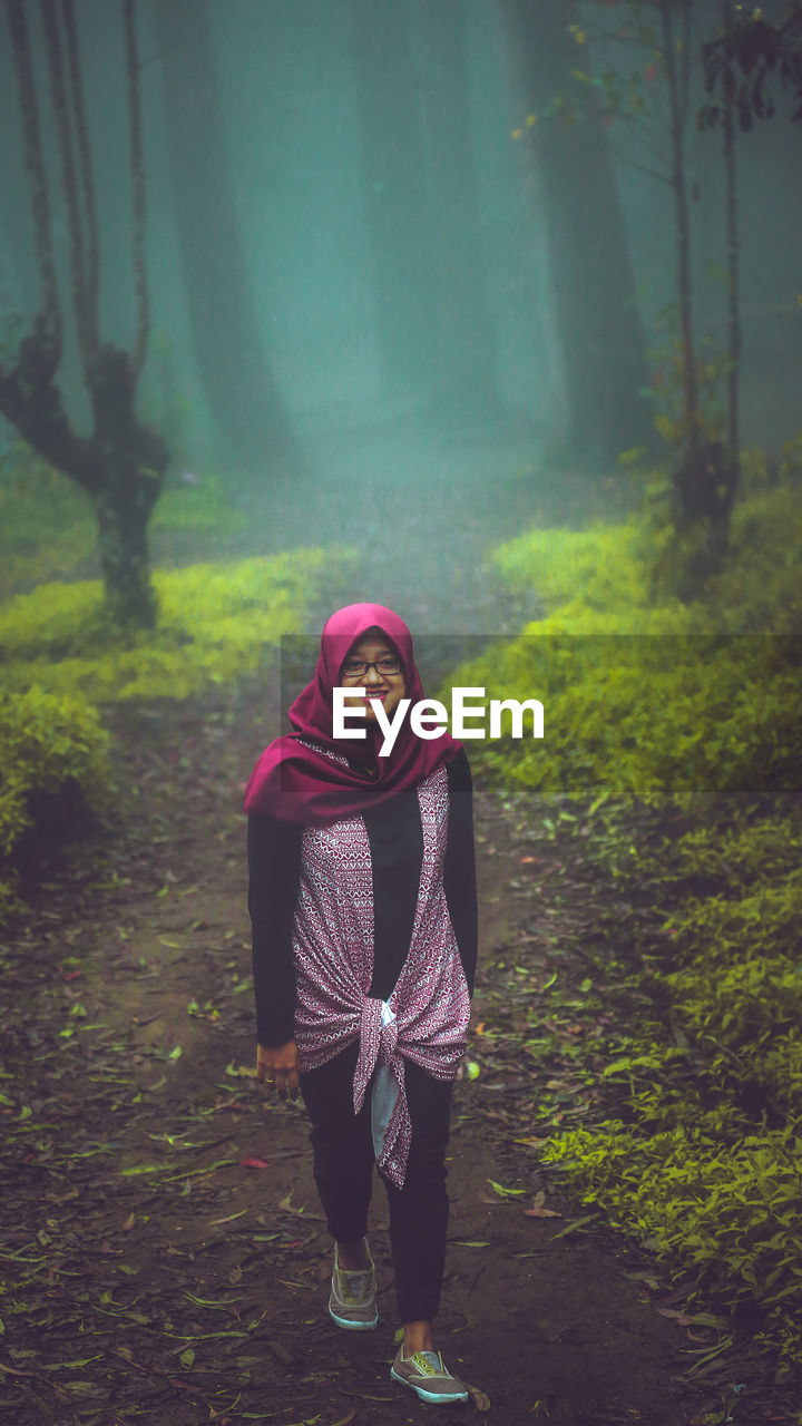 Portrait of young woman wearing hijab while walking in forest