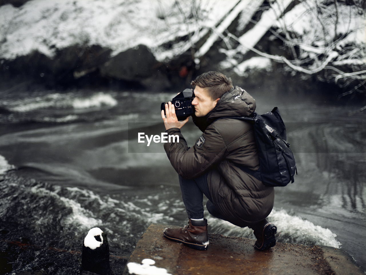 Profile view of man photographing with camera at riverbank during winter