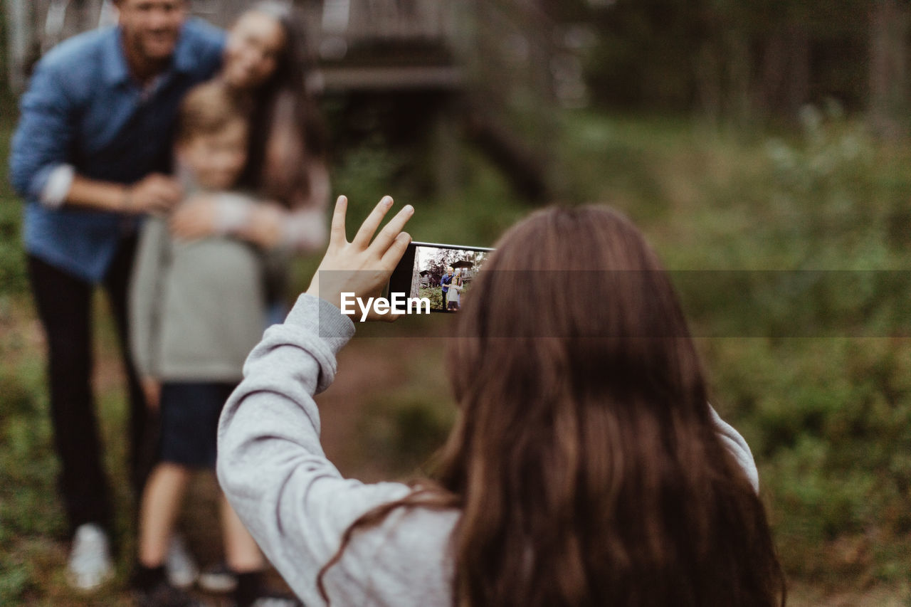 Girl taking picture of family with mobile phone while standing in backyard