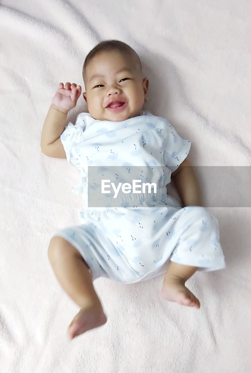 baby, child, childhood, one person, innocence, full length, cute, indoors, baby clothing, bed, babyhood, high angle view, person, lying down, beginnings, portrait, relaxation, lying on back, clothing, emotion, toddler, happiness, front view, furniture, newborn, directly above, smiling, barefoot, white, textile, bedroom, cheerful, comfortable, fragility, joy, positive emotion, linen, mouth open, looking, nature, looking at camera