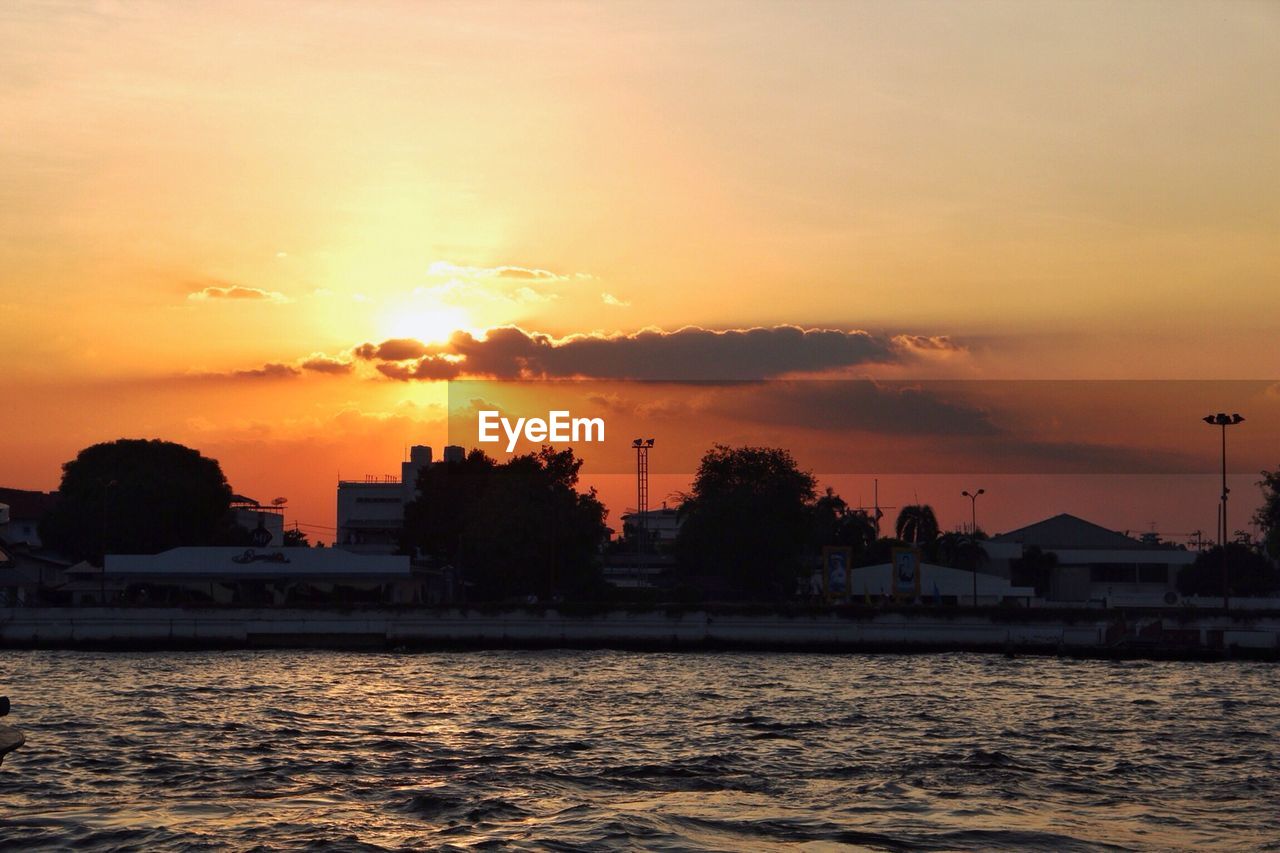 Cityscape by chao phraya river against sky during sunset