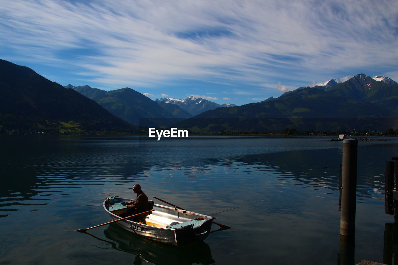 BOAT MOORED IN LAKE AGAINST MOUNTAINS