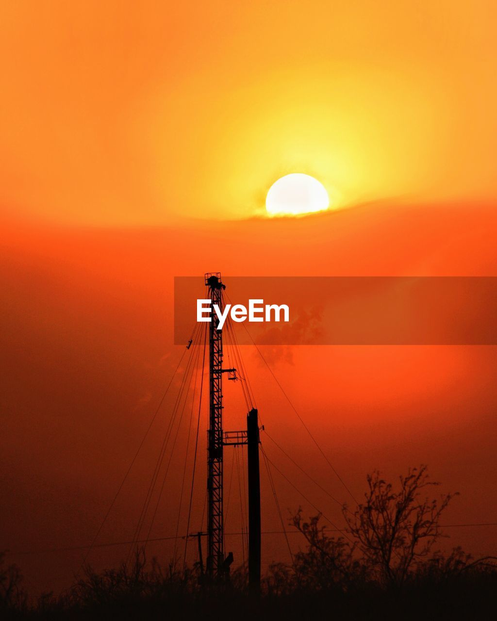 Silhouette oil pump against orange sky during sunset