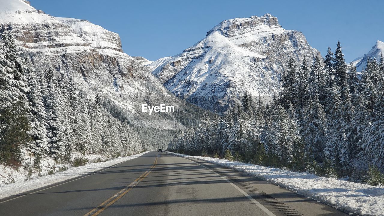 Empty road amidst snowcapped mountains during winter