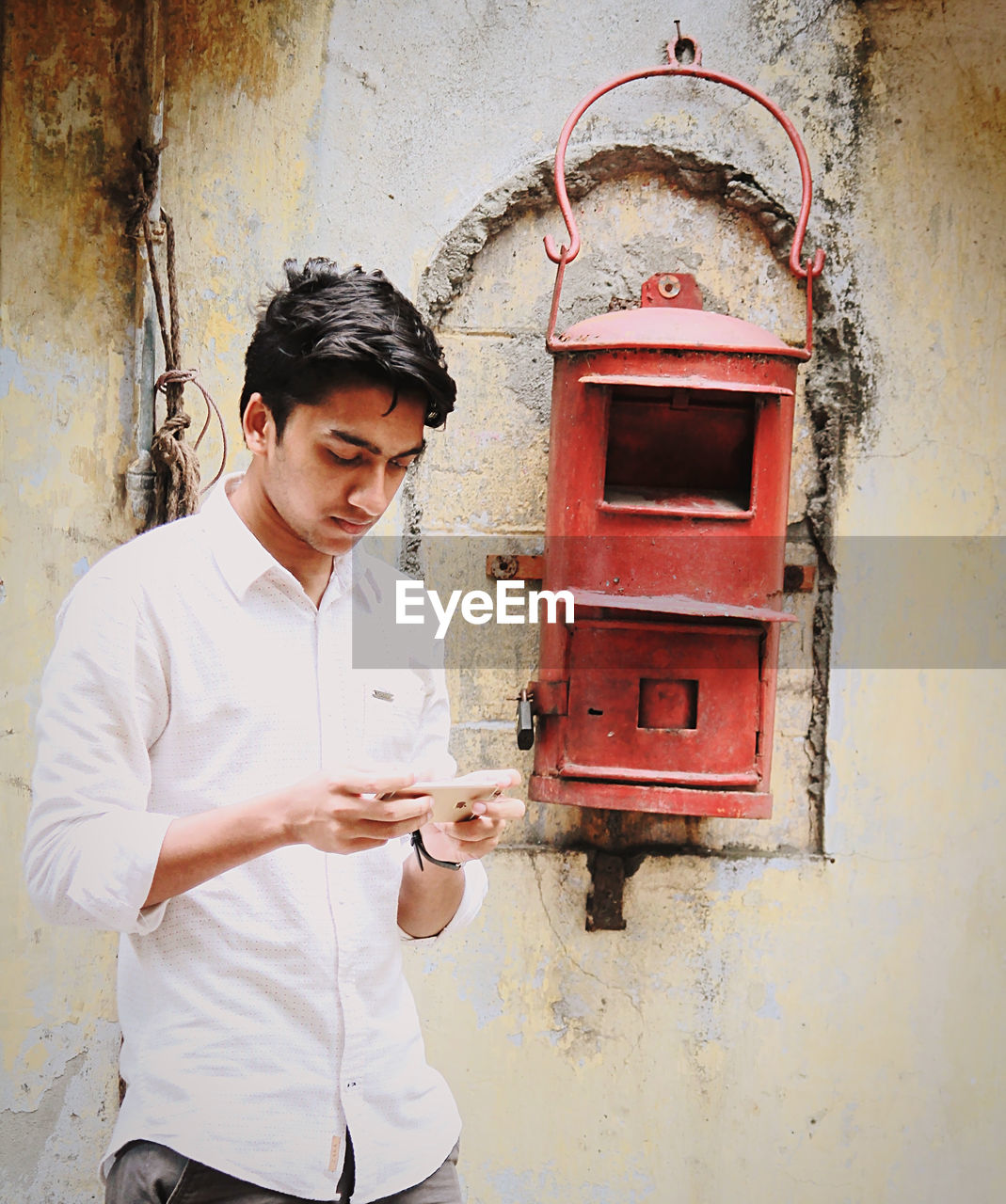 Young man using smart phone while standing against wall