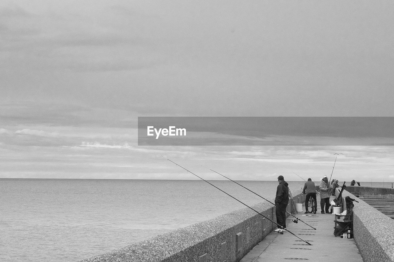 People fishing in sea against sky