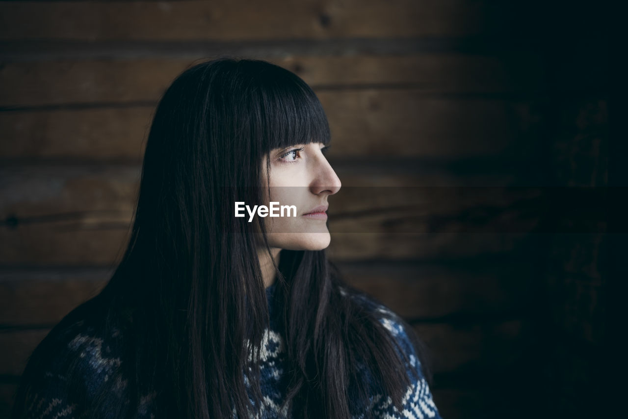 Close-up of thoughtful woman looking away at log cabin