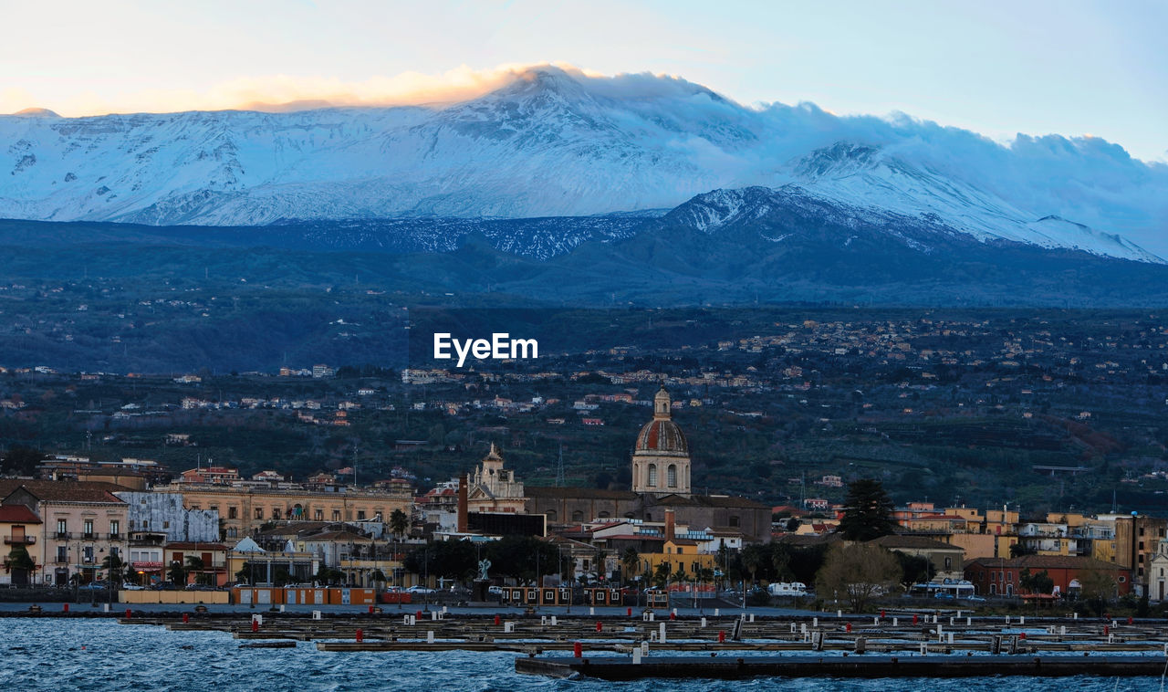 Aerial view of the cityscape and etna volcano against the sky