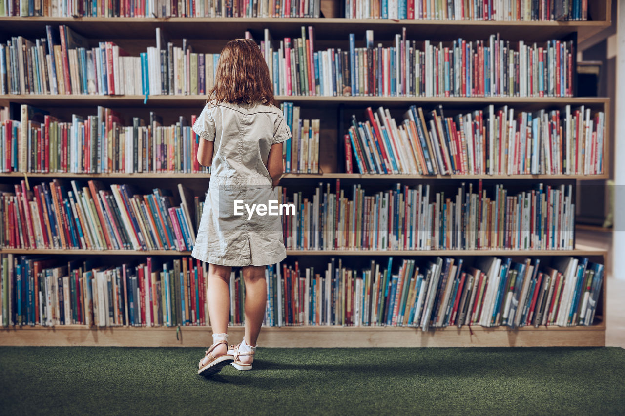 Student choosing book in school library. girl selecting literature for reading. books on shelves