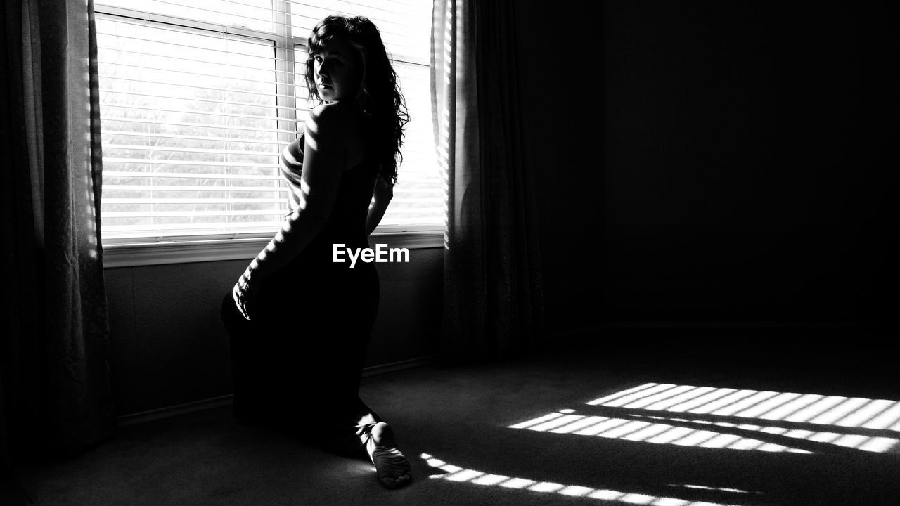 Portrait of woman sitting by window at home on sunny day