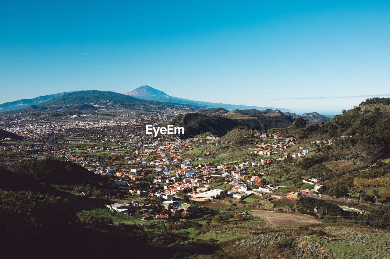 Aerial view of townscape and mountains against clear blue sky