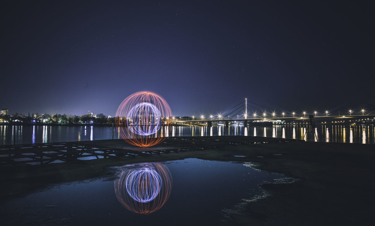 Illuminated light trail by river at night