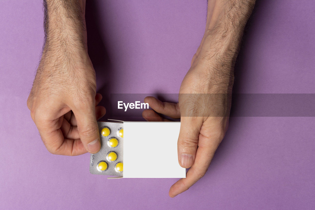 Male hand bringing out pills tablet from box in front of purple background, selection path icluded.