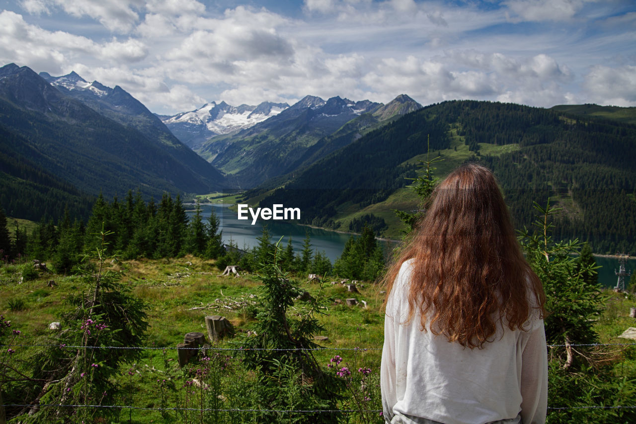 Rear view of woman looking at mountains against cloudy sky