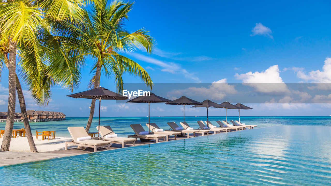 Luxury resort poolside with beach view, horizon and blue sunny sky. luxury vacation chairs umbrellas