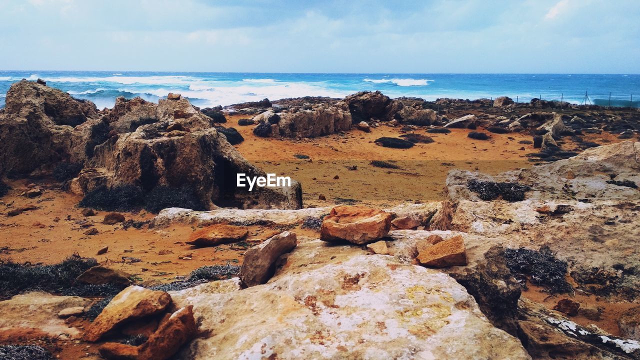 Scenic view of rocks on shore against sky