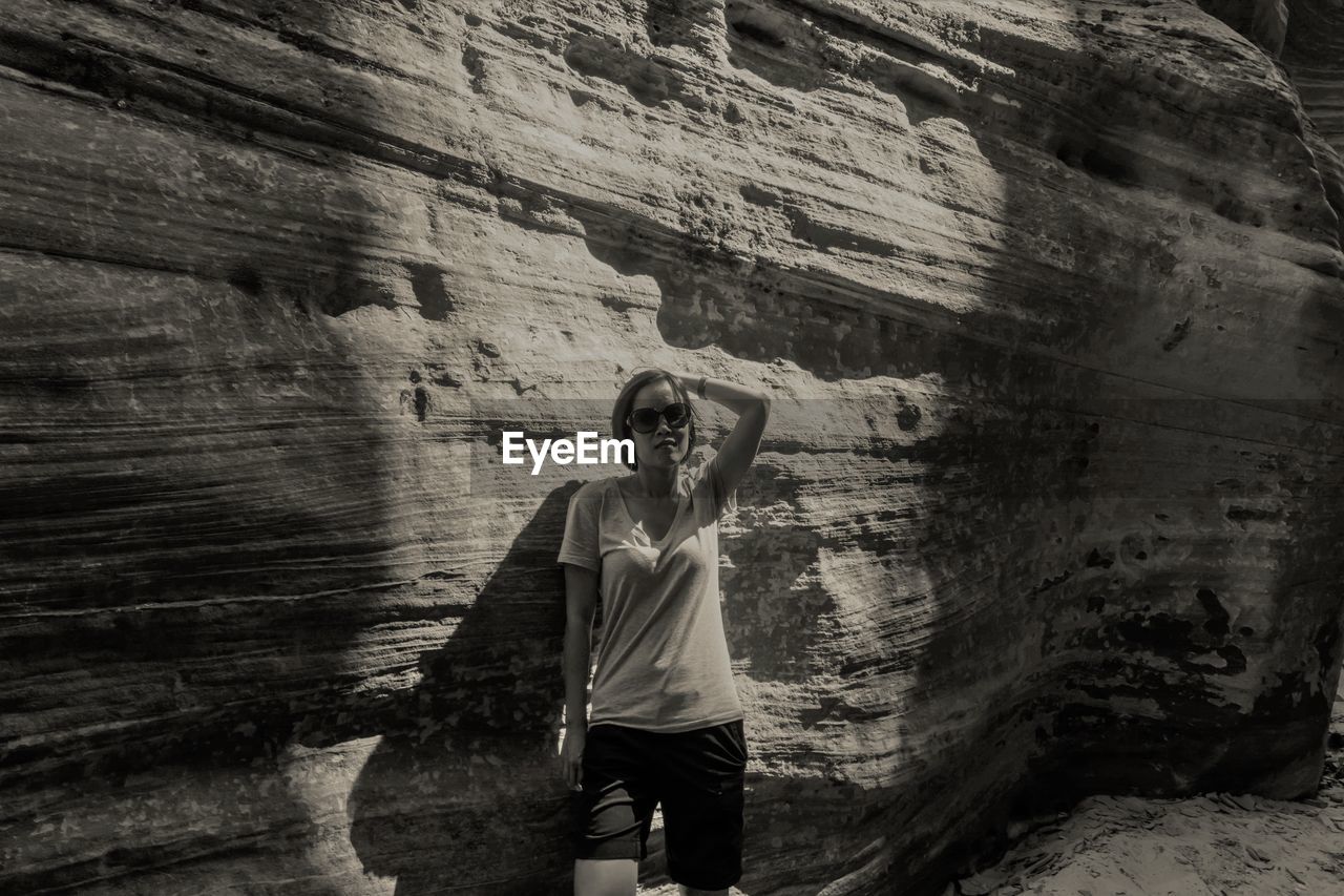 Portrait of woman wearing sunglasses standing against rock formation