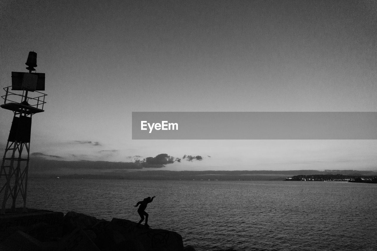 Silhouette person standing on rocks by sea against sky during sunset