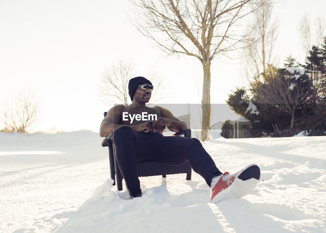 Shirtless sportsman relaxing while sitting on chair during winter