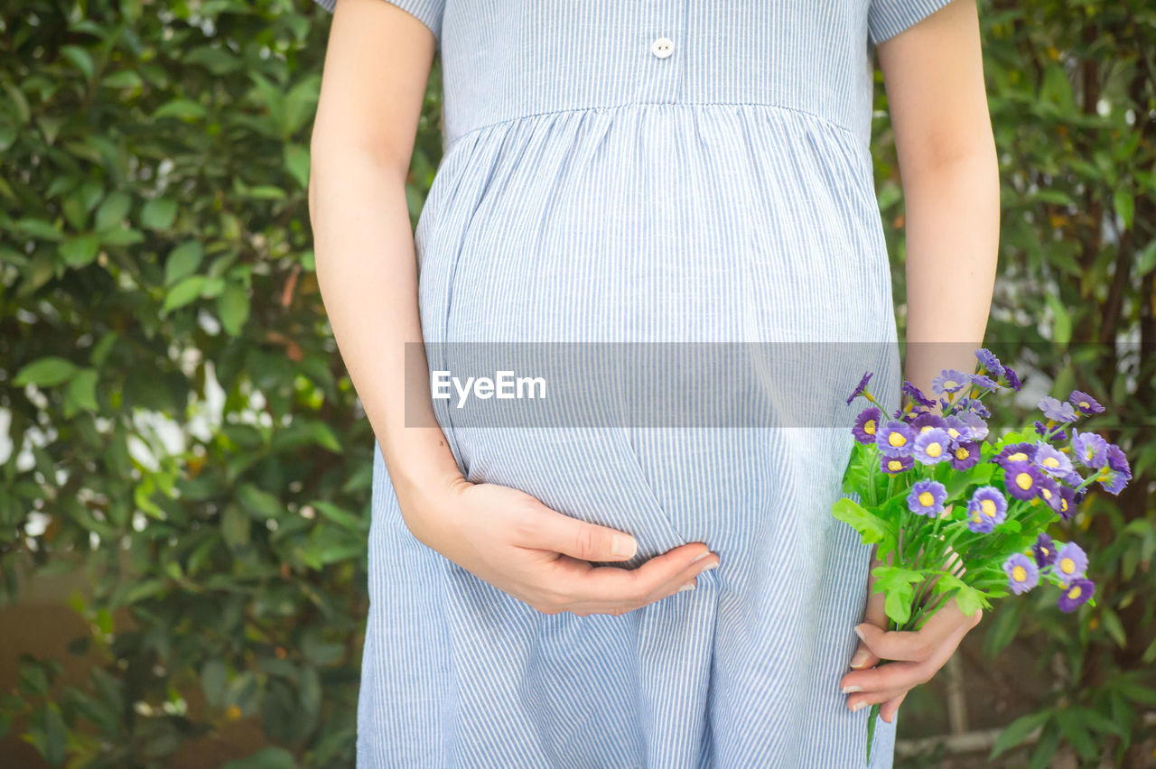 Midsection of pregnant woman holding flowers while standing at park