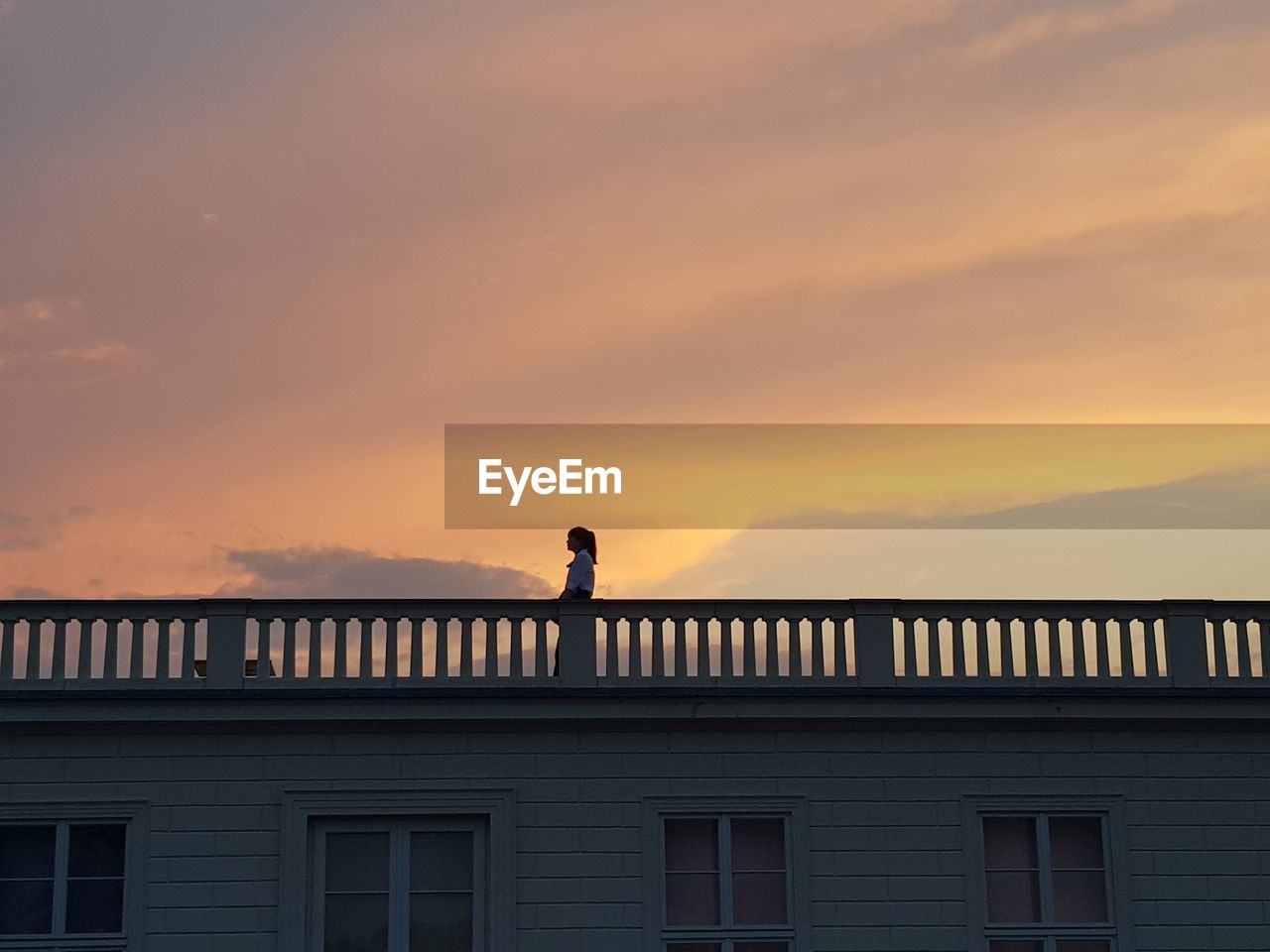 Low angle view of woman standing in balcony against sky during sunset