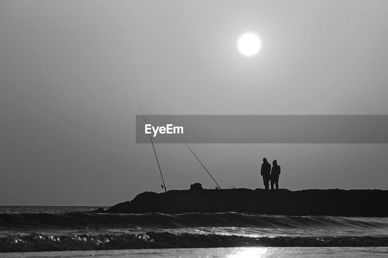 Silhouette people fishing in sea against clear sky