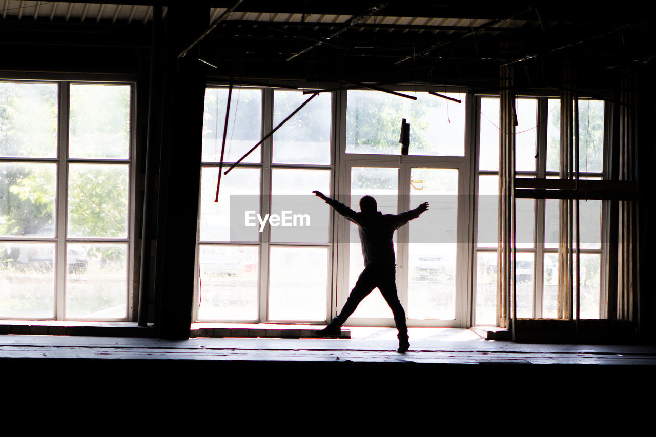 Man with arms outstretched standing by window