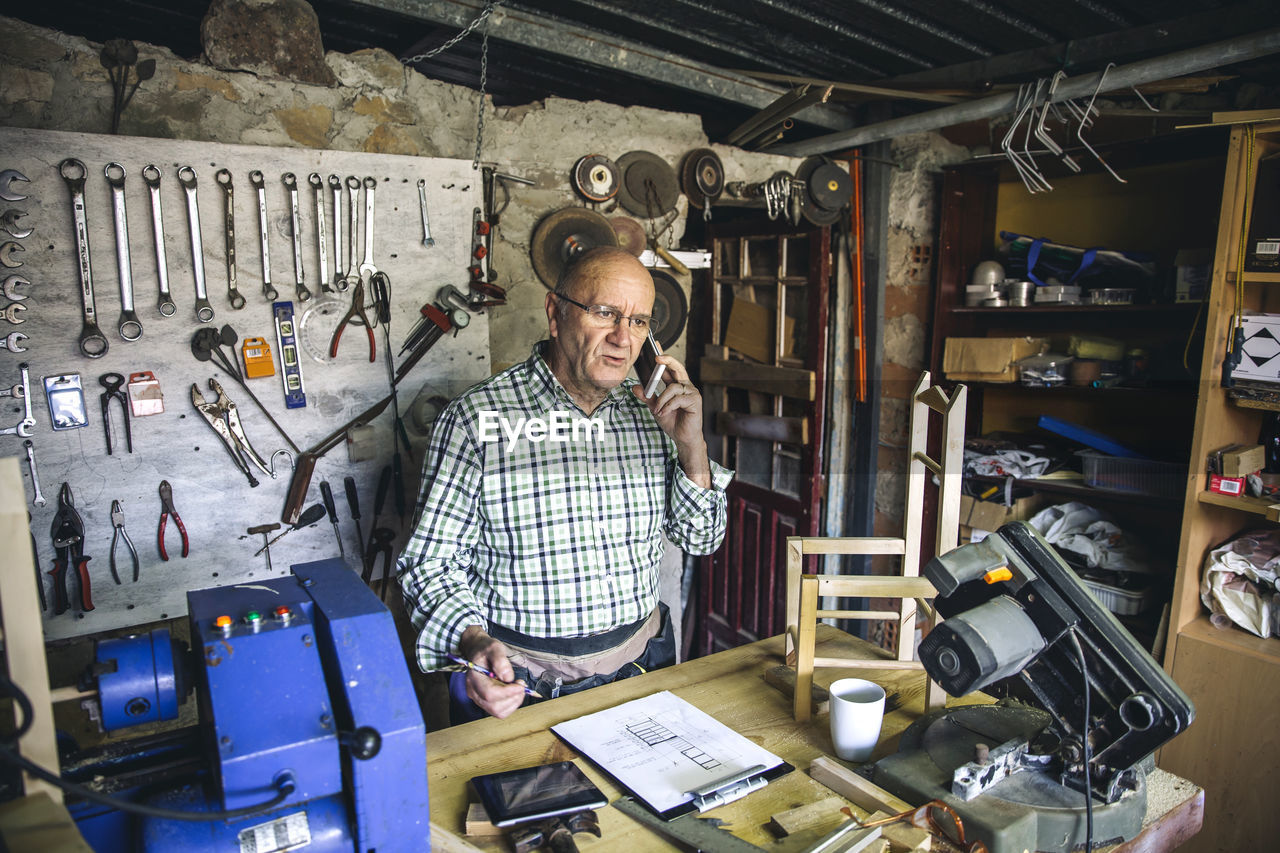 Man talking over smart phone while standing in workshop