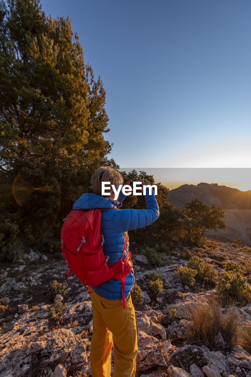 Woman hiking and taking a picture of the puig campana mountains.