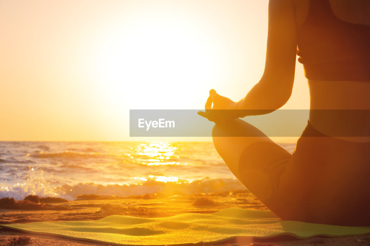 Close-up yoga woman meditating at serene sunset or sunrise on the beach. the girl relaxes in the