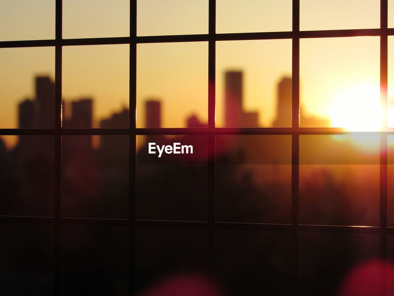 Silhouette buildings seen through glass window during sunset