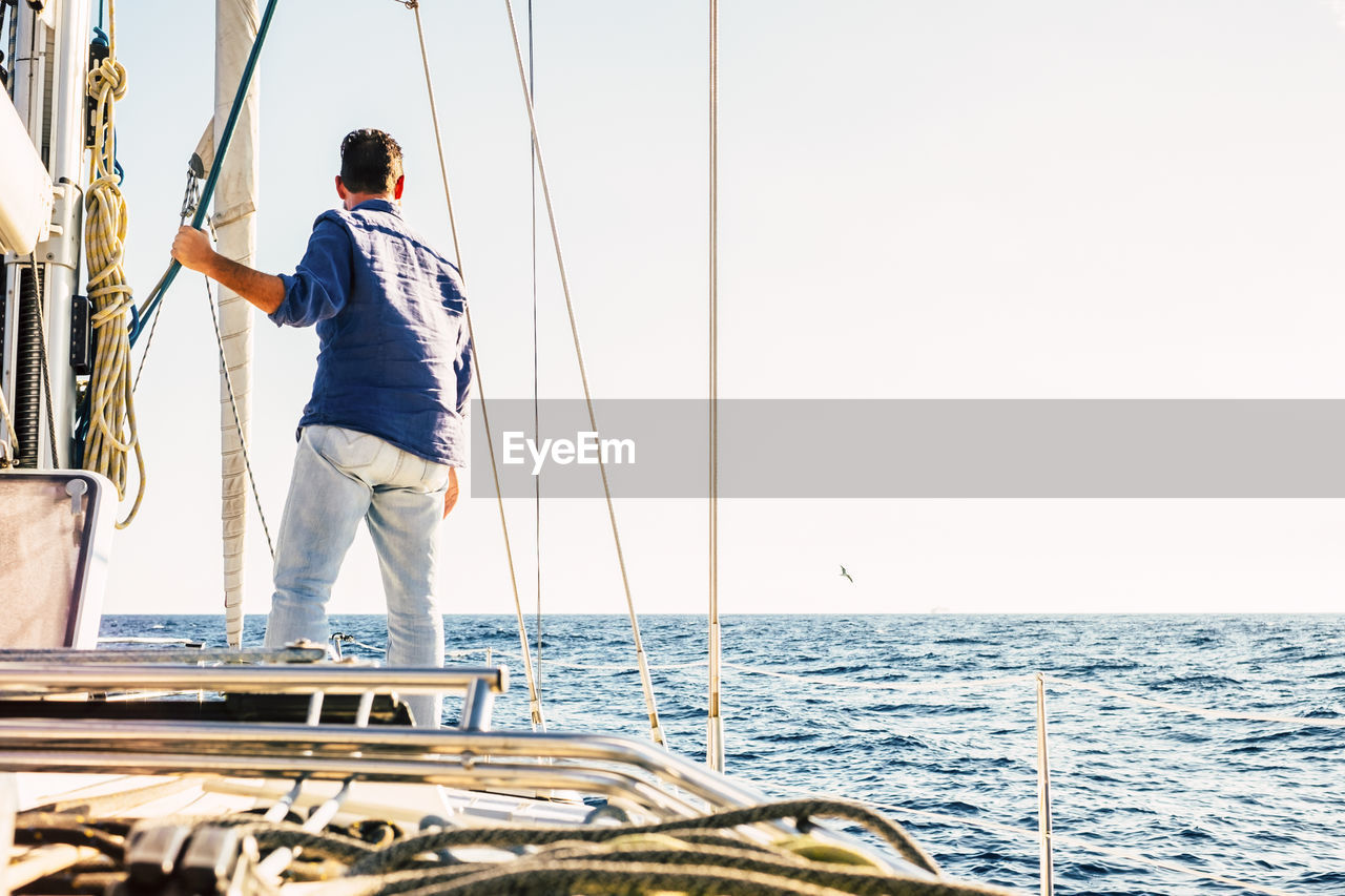 Rear view of man standing on boat in sea against clear sky