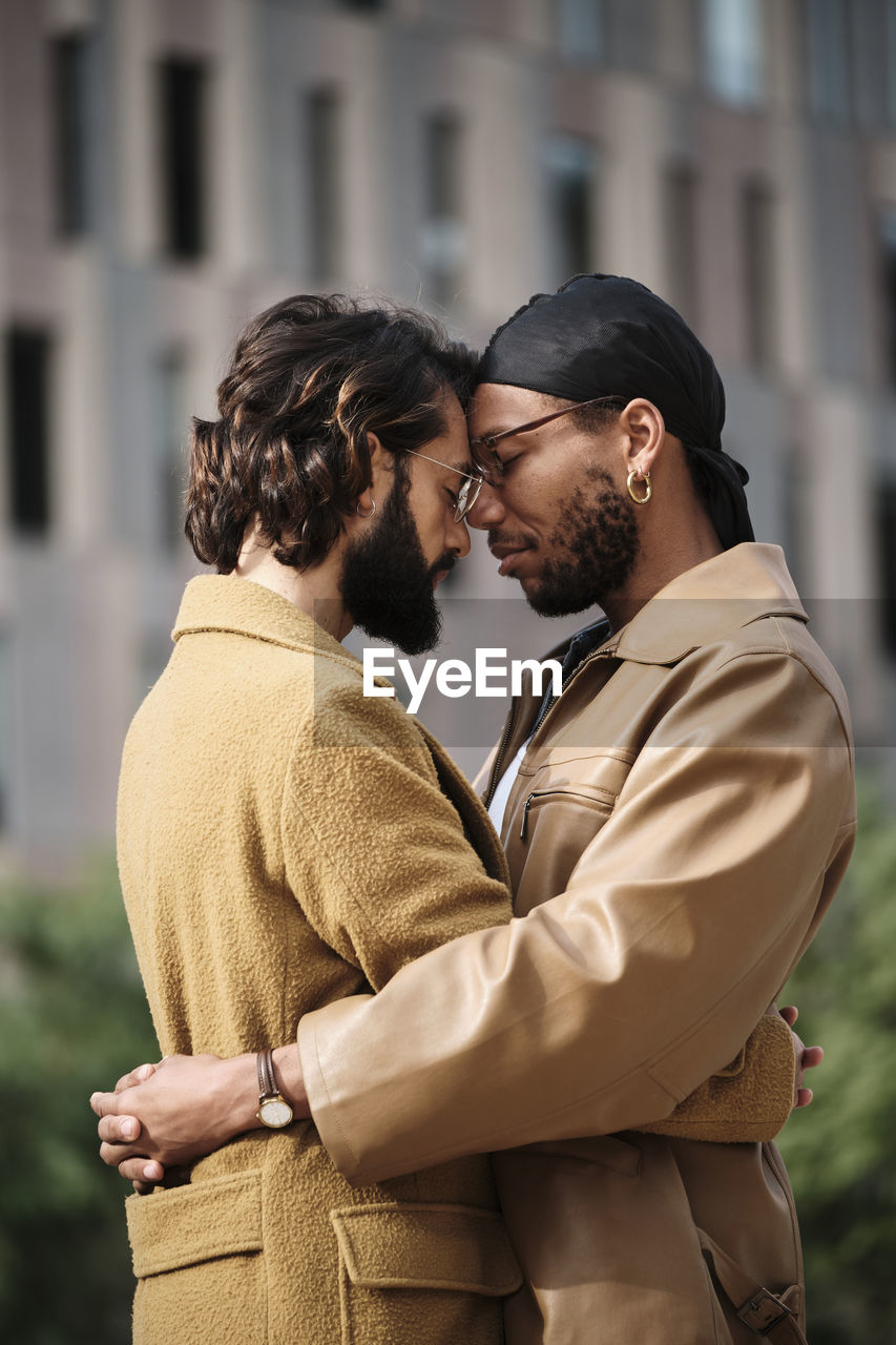 Gay couple with eyes closed embracing each other outside building