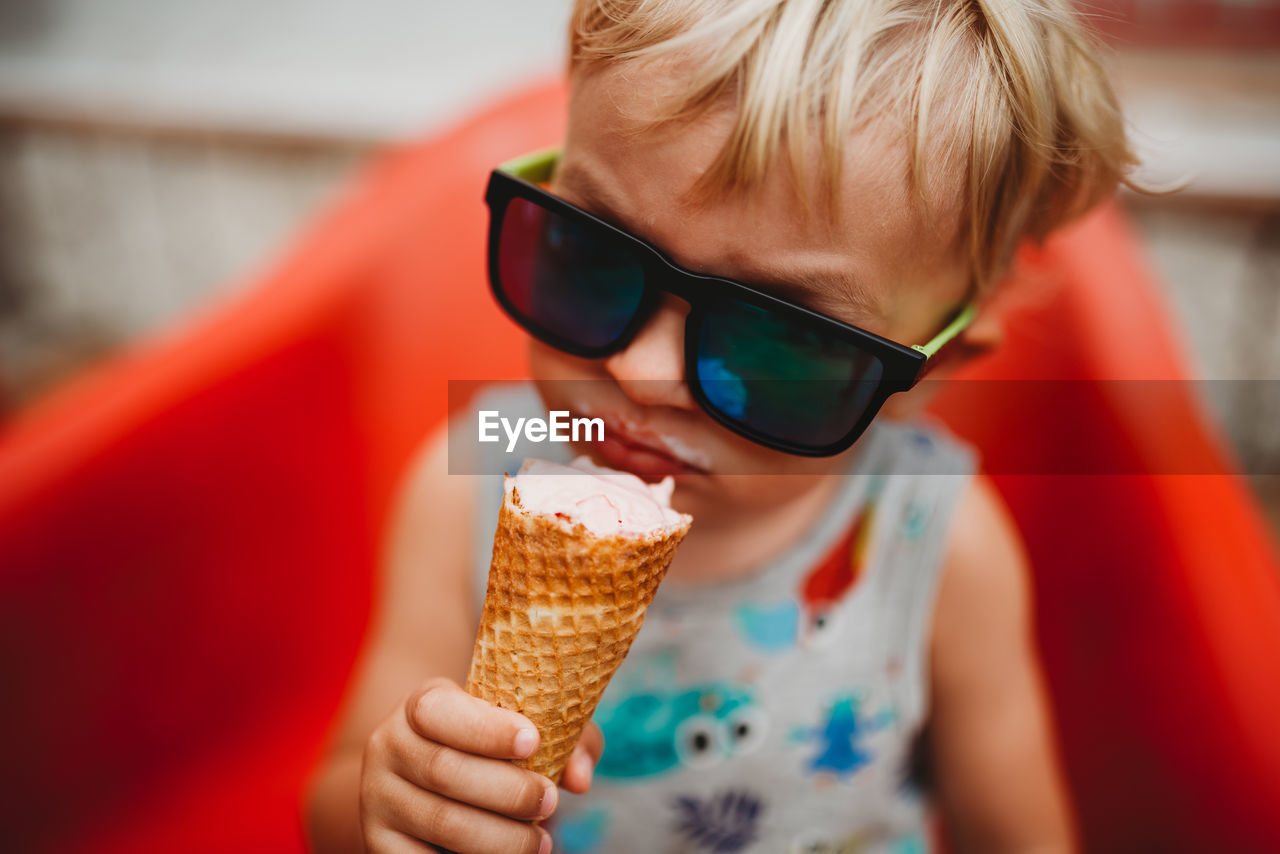 White blonde toddler eating ice cream cone with sunglasses