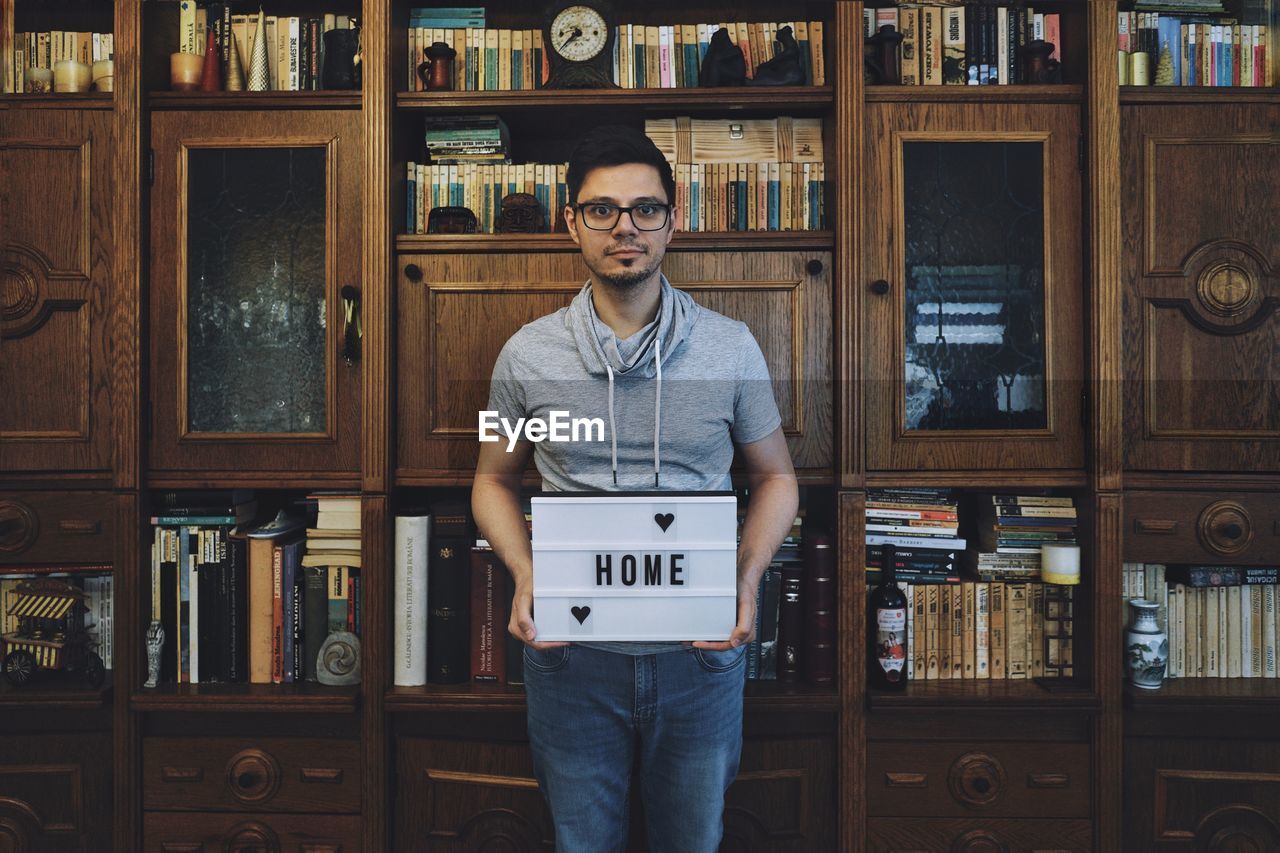 Portrait of man holding home text against shelves