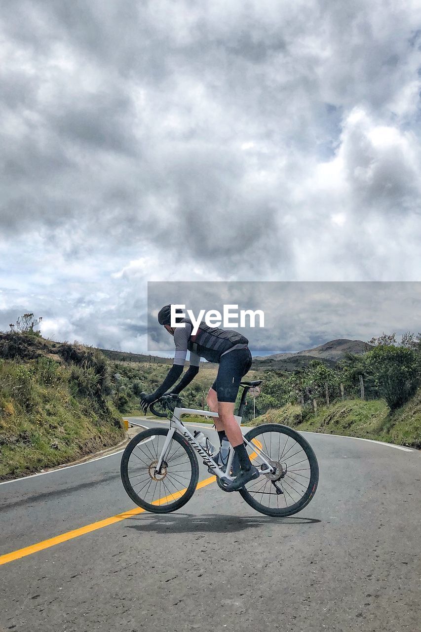 PERSON RIDING BICYCLE ON ROAD AGAINST SKY